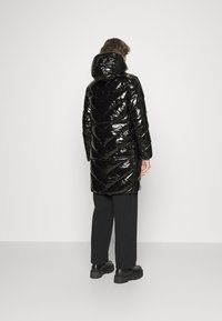 Svart, glänsande pufferjacka med huva, med ett chevronmönster och långa ärmar. Bärs med svarta byxor och skor med kraftig sula.