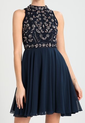 Mouwloze marineblauwe jurk met hoge halslijn, bloemrijke paillettenborduursel op het lijfje, getailleerde taille en vloeiende knielange rok.