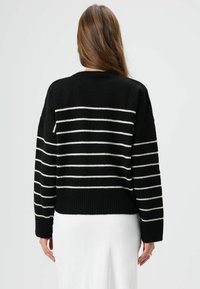 Pull en maille noire avec des rayures horizontales blanches, ourlet côtelé et manches longues. Le dos présente un col rond classique.