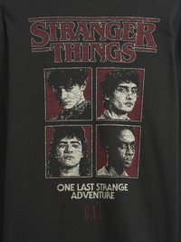 Tricou negru din bumbac cu un grafic imprimat serigrafic reprezentând patru personaje în roșu și alb, cu legenda „O ULTIMĂ AVENTURĂ STRANIE” și logo-ul mărcii.