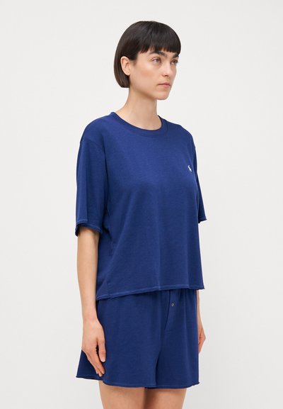 Mörkblå bomulls t-shirt med kort ärm och rund halsringning, prydd med en liten logotyp på bröstet, matchad med mörkblå shorts med en knapp.