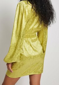 Kort gul klänning med långa puffärmar; har ett texturerat blommönster och en elastisk midja för en figurnära silhuett.