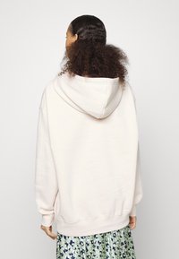 Sudadera rosa claro con un diseño amplio, textura suave y una gran capucha. Presenta mangas raglán y puños y dobladillo de canalé.
