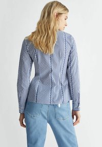 Blusa a righe blu e bianche con maniche lunghe, caratterizzata da una banda di design verticale centrale, in cotone e con una silhouette aderente.