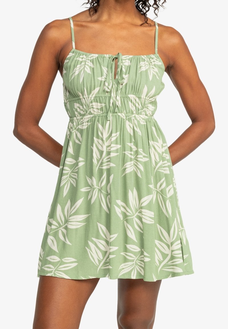 Vihreä mekko, jossa on lehtikuosi, kevyt materiaali, spagettiolkaimet, istuva yläosa joustavalla nauhalla, polviin asti ulottuva pituus ja nyörielementti kaula-aukossa.