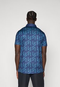 Koszulka polo z krótkim rękawem w granatowym kolorze z fakturą wzoru w jasnoniebieskie litery "LS" i "1." Posiada kołnierzyk i lekko zaokrąglony dół.