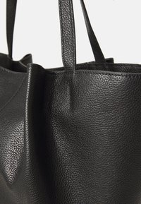 Borsa tote in pelle nera con finitura testurizzata, dotata di due manici robusti e un design spazioso e aperto. Edges minimalisti e senza cuciture.
