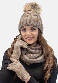 Căciulă tricotată bej cu un pompon din blană sintetică, asociată cu o eșarfă și mănuși bej, având un model texturat și manșete cu dungi.