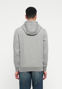 Gray hoodie made of soft fabric, featuring a drawstring hood, ribbed cuffs, and hem. Worn over denim jeans, viewed from the back.