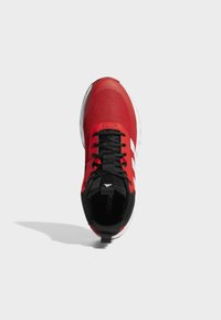 Zapatilla deportiva roja con parte superior de malla, cordones negros y acentos blancos. Cuenta con una suela acolchada y una pestaña en el talón.