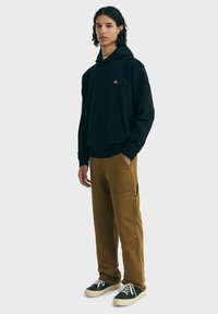 Čierna mikina s kapucňou a klokankovým vreckom, kombinovaná s hnedými cargo nohavicami so bočnými vreckami a striebornými kovaniami, nosená s čiernymi teniskami.