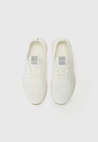 White athletic shoes made of knit material, featuring a textured pattern, flexible sole, and a branded tag on the tongue.
