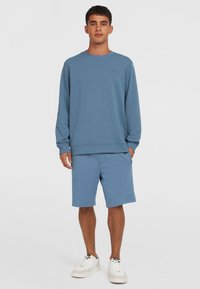Lyseblå bomulds sweatshirt med lange ærmer og ribbede manchetter, parret med matchende shorts. Sneakers har hvid overdel og strukturerede detaljer.