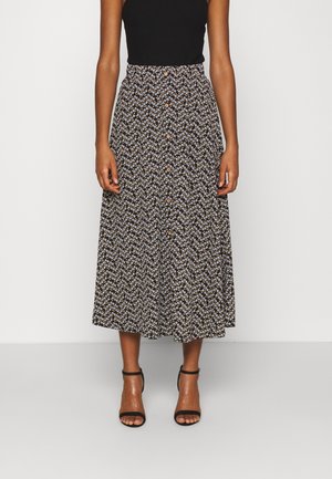 Schwarzer, knielanger Rock mit weißen Blumenmuster und braunen Knöpfen vorne. Kombiniert mit einem enganliegenden schwarzen Oberteil und schwarzen Sandalen mit Riemchen.