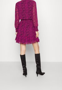 Vestido de estampado rosa y negro con dobladillo con volantes y mangas largas, combinado con botas altas negras de tacón. Textura suave y diseño fluido.