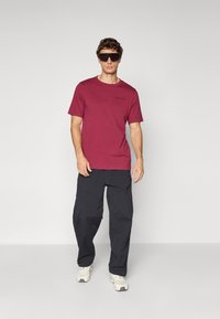 Maroon short-sleeve t-shirt with a round neckline and logo detail, paired with black cargo pants featuring multiple pockets and a loose fit.