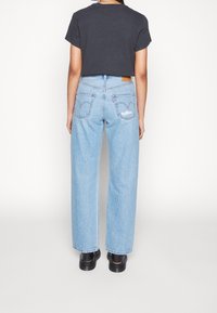 Ljusblå högmidjade jeans med rak benlängd och subtil slitning på bakfickorna. Kombinerat med en svart kortärmad t-shirt.