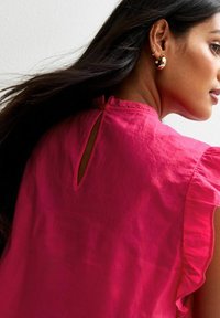 Roze linnen blouse met ruches aan de mouwen, een sleutelgatdetail op de rug en een gladde textuur.