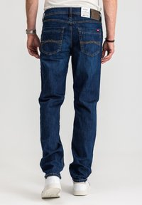 Dopasowane ciemnoniebieskie dżinsy o średnim stanie, z dwiema tylnymi kieszeniami z ozdobnym przeszyciem oraz skórzaną naszywką marki na pasku.