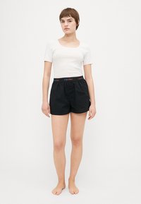 Crni pamučni bokserice s elastičnom trakicom koja ima višebojni Calvin Klein logo, uparen s prilagođenim bijelim majicom kratkih rukava.