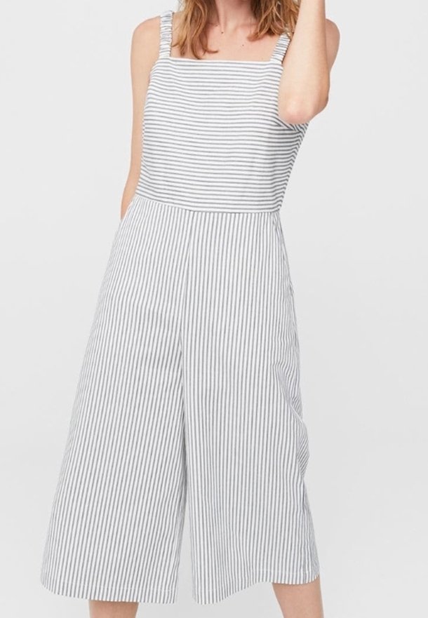 Femme portant une combinaison sans manches à jambes larges avec des rayures verticales et horizontales grises et blanches, debout devant un fond uni.