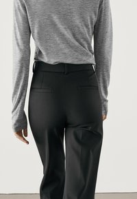 Pantalons noirs avec une coupe ajustée, présentant une texture lisse, des poches arrière et une large ceinture, assortis à un haut gris à manches longues.
