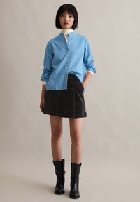 Lichtblauw gestreept shirt met een staande kraag, zwarte geplisseerde rok en kniehoge zwarte laarzen. Glad stof en gestructureerd ontwerp.