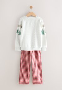 Børnetøj med en hvid sweatshirt med grønne fyrretræer og bjergmotiver på ærmerne, kombineret med røde og hvide ternede bukser.