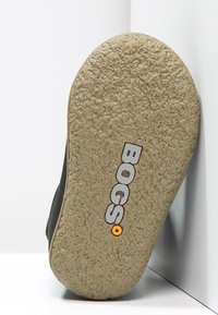 Suela de goma negra con superficie texturizada, presenta el logotipo "BOGS" en gris y naranja. Forma redondeada, diseñada para tracción y durabilidad.
