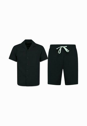 Zwart kort mouw overhemd met knopen en kraag, gecombineerd met zwarte shorts met trekkoord en witte strikjes, weergegeven op een witte achtergrond.