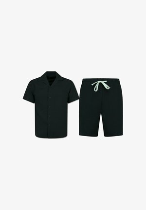 Zwart kort mouw overhemd met knopen en kraag, gecombineerd met zwarte shorts met trekkoord en witte strikjes, weergegeven op een witte achtergrond.