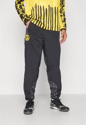 Zwarte sportpant met een glanzende afwerking, met een schedelpatroon op de onderbenen en een gele BVB-logo op de bovenbenen.