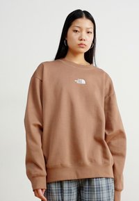 Hnědá oversized mikina vyrobená z bavlněné směsi, s kulatým výstřihem a logem The North Face na hrudi, s dlouhými rukávy a žebrovanými manžetami.