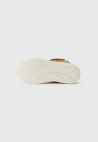 Semelle en caoutchouc de couleur claire avec un grip texturé. La tige est en cuir marron avec une sangle Velcro. Le design est simple et fonctionnel.