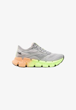 Lichtgrijze Reebok hardloopschoen met mesh bovenwerk, patroonveters en een dikke zool die oranje is bij de hiel en neon groen aan de voorkant.
