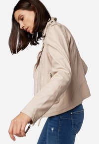 Ljus beige läderjacka med en figurnära design, dragkedjestängning och subtila sömnadsdetaljer, kombinerad med blå denimjeans.