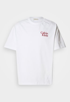 Valge puuvillane T-särk, millel on ümar kaelus, lühikesed varrukad ja punane tikand "Calvin Klein" logo rinnal.