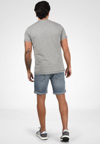 Pelēks īsām piedurknēm t-krekls, kas saskaņots ar sarullētiem džinsiem šortiem. Apavi ar pelēku un baltu dizainu ar svītrām. Vienkāršs, ikdienišķs izskats.