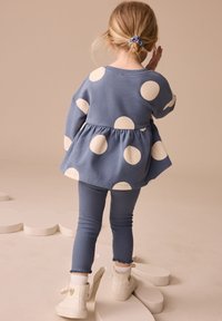 Sinine polka dot peplum lõhikuga top, millel on pikad varrukad, koos ribatud siniste retuusidega ja valgete kingadega. Topil on märgatavad ümmargused valged täpid.