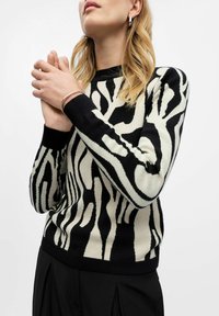 Pull rayé noir et crème au design ajusté, avec des manches et un ourlet côtelés. Modèle portant de simples accessoires en argent.