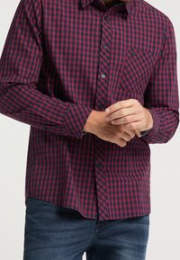 Czerwona i granatowa koszula w kratę zapinana na guziki z kołnierzykiem, długimi rękawami i jedną kieszonką na piersi. Wykonana z lekkiego materiału o gładkiej fakturze.