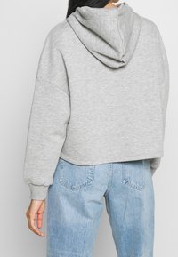 Persona che indossa un crop hoodie grigio chiaro e jeans a vita alta blu chiaro, vista di schiena su uno sfondo semplice.