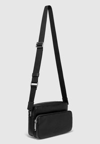 Svart axelväska i texturerad läder, med två blixtlåsfack och en justerbar textilrem.