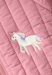Un tissu matelassé rose présente une licorne blanche brodée avec une crinière et une queue pastels, placée sur un fond à la texture douce.