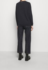 Tmavá mikina s dlouhými rukávy a žebrovanými manžetami, ve spojení s volně střiženými tmavými džíny. Černé kotníkové boty dotvářejí tento outfit.