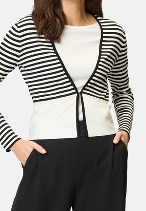 Cardigan rayé en noir et blanc avec un col en V et un devant fendu. Il a des manches longues et une texture lisse et douce. Assorti à un pantalon noir.