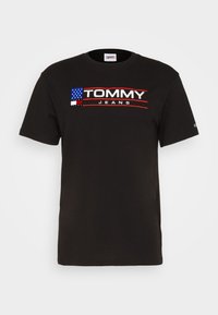 Černé bavlněné tričko s červeným a bílým logem "TOMMY JEANS", doplněné modrým designem americké vlajky na levé straně hrudi.