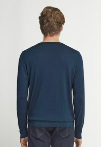 Mörkblå långärmad tröja med rundad hals, tillverkad av ett mjukt stickat material, med ribbade manschetter och nederkant, samt en slät yta.