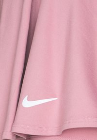 Camisa atlética de color rosa claro, hecha de una tela suave, que presenta un logotipo de Nike en blanco en la parte inferior izquierda y bordes lisos y de corte regular.
