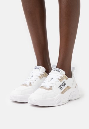 Białe sneakersy z masywną podeszwą, ozdobione złotymi brokatowymi akcentami i detalami z logo. Gładka skórzana faktura z wiązaniem na sznurowadła.